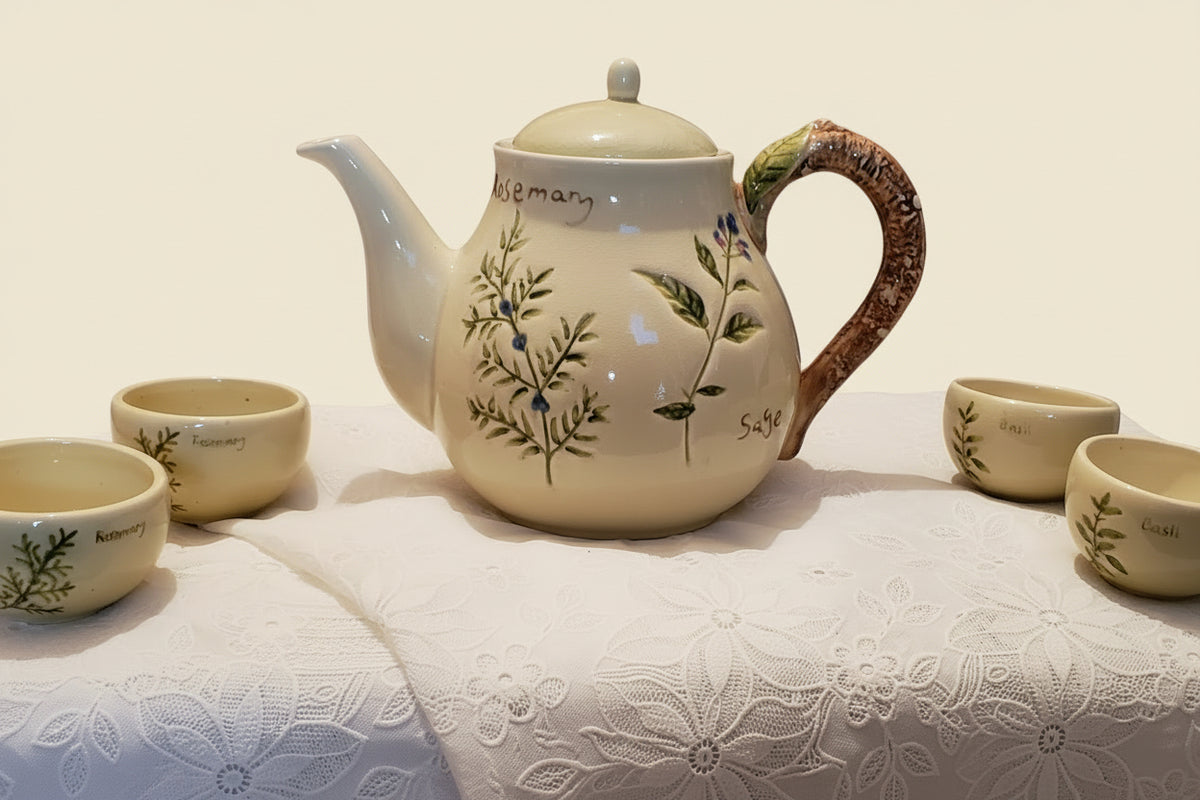 Ceramic teapot and cups with floral design on a tablecloth.